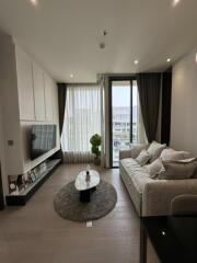 Modern living room with a large sofa, mounted TV, and large window with sheer curtains