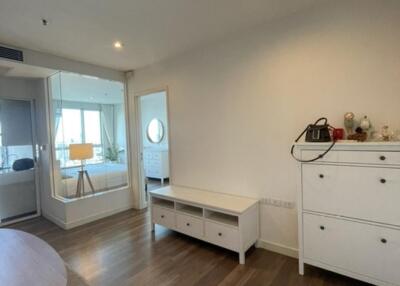 Living room with wooden floor, storage cabinets, and a glimpse of a bedroom in the background