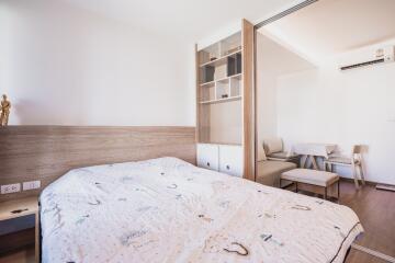 Bright bedroom with white bedding and wooden accents leading to a living area