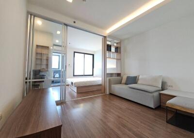 Modern living area with wooden floor and view into bedroom through glass sliding door