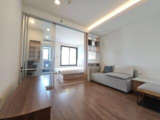 Modern living area with wooden floor and view into bedroom through glass sliding door