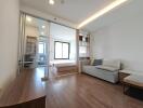 Modern living area with wooden floor and view into bedroom through glass sliding door