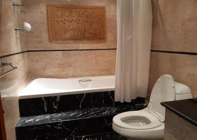 Bathroom with beige marble walls, black stone bathtub steps, and a modern toilet