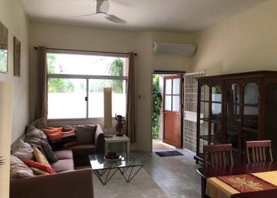 Living room with brown sofa, glass coffee table, wooden cabinet, dining table, and a door leading outside