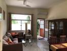 Living room with brown sofa, glass coffee table, wooden cabinet, dining table, and a door leading outside