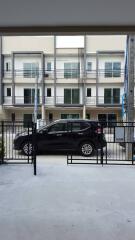 View of a townhouse building with multiple floors and balconies, seen from a driveway with a parked black car in front