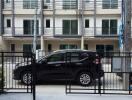 View of a townhouse building with multiple floors and balconies, seen from a driveway with a parked black car in front