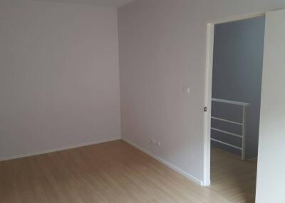 Empty bedroom with light colored laminate flooring and an open door leading to a small landing area