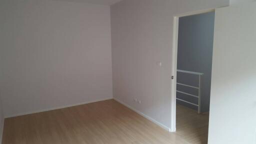 Empty bedroom with light colored laminate flooring and an open door leading to a small landing area