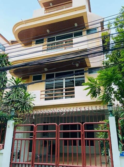 Front view of a multi-story residential building with a gated entrance and surrounding greenery