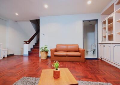 Living room with wooden floor, brown sofa, and staircase