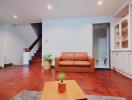 Living room with wooden floor, brown sofa, and staircase