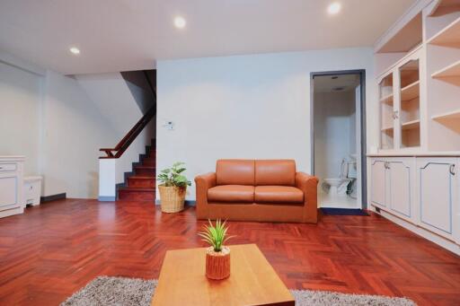 Living room with wooden floor, brown sofa, and staircase