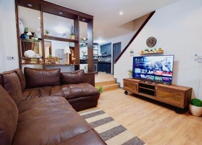 Living room with a brown leather sofa, wooden TV stand, and a view of the kitchen area