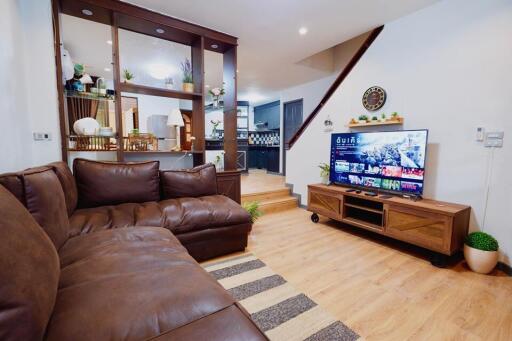 Living room with a brown leather sofa, wooden TV stand, and a view of the kitchen area