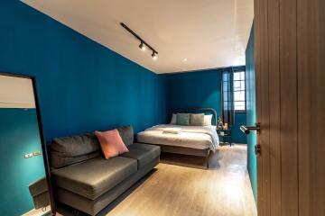 Modern bedroom with blue walls, a bed, and a sofa