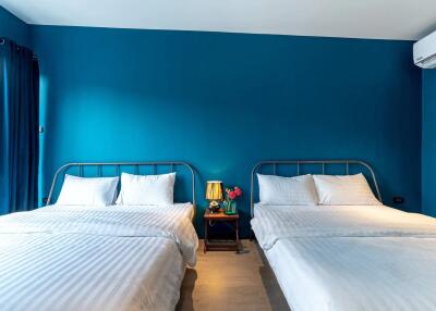 Bedroom with two double beds, blue walls, white bedding, and air conditioning