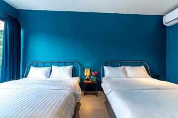 Bedroom with two double beds, blue walls, white bedding, and air conditioning