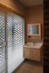 Modern bathroom with sink and mirror, natural light from large window with blinds