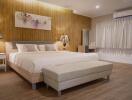 Spacious bedroom with a bed, nightstands, lamps, wooden accent wall, air conditioning, and bench