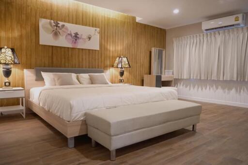 Spacious bedroom with a bed, nightstands, lamps, wooden accent wall, air conditioning, and bench