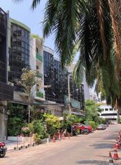 Street view of a commercial building with greenery and parked vehicles