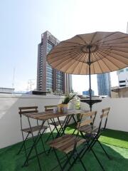 Outdoor dining area with table and chairs under an umbrella on an artificial grass surface