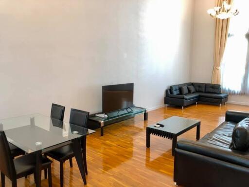 Spacious modern living room with hardwood floors, black leather furniture, and a glass dining table