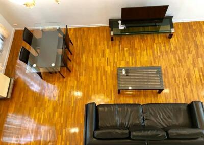 Modern living room with wooden flooring, black leather sofa, glass dining table, and TV setup