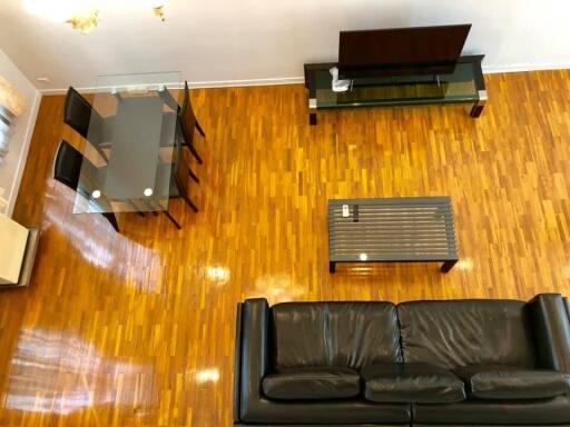 Modern living room with wooden flooring, black leather sofa, glass dining table, and TV setup