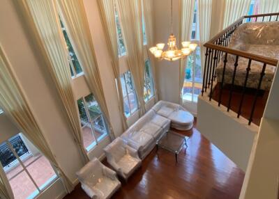 Spacious double-height living room with large windows, hardwood floors, and elegant chandelier