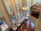 Spacious double-height living room with large windows, hardwood floors, and elegant chandelier