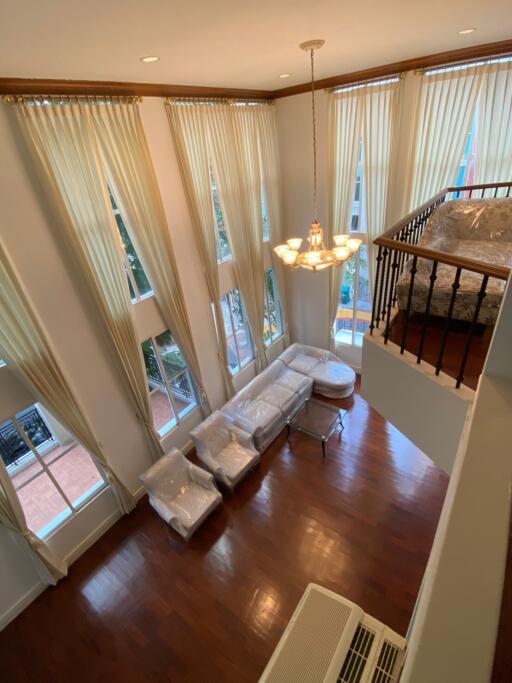 Spacious double-height living room with large windows, hardwood floors, and elegant chandelier