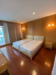 Spacious bedroom with twin beds, wooden flooring, and wall-mounted lighting