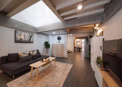 Modern living room with skylight, grey sofa, wooden furniture, and wall-mounted TV.