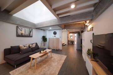 Modern living room with skylight, grey sofa, wooden furniture, and wall-mounted TV.