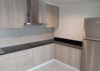 Modern kitchen with light wood cabinets, black countertop, and stainless steel appliances