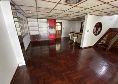 Spacious living area with wooden flooring, leading to kitchen and stairway