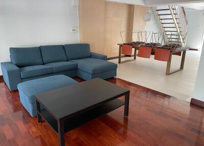 Modern living room with blue sectional sofa and black coffee table near dining area and staircase