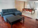 Modern living room with blue sectional sofa and black coffee table near dining area and staircase