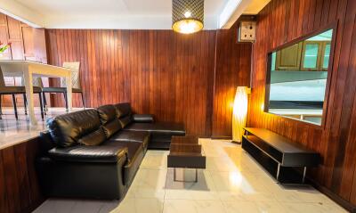 Cozy living room with wooden panel walls and black leather furniture