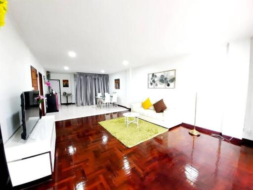 Spacious living room with white sofa, colorful cushions, and wooden flooring