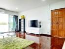 Modern living room with a TV, wooden flooring, and balcony access