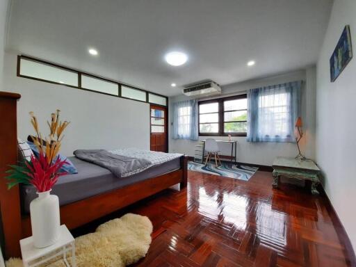 Spacious bedroom with polished wooden flooring, large windows, and modern furniture