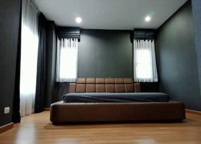 Modern master bedroom with large bed, stylish dark walls, and wooden flooring.