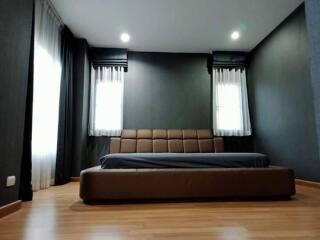 Modern master bedroom with large bed, stylish dark walls, and wooden flooring.