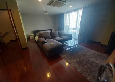 Living room with hardwood floors, L-shaped sofa, and large windows with curtains