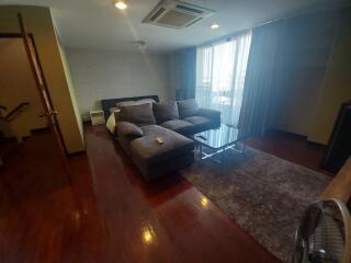 Living room with hardwood floors, L-shaped sofa, and large windows with curtains