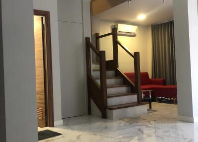 Spacious living room with marble flooring, modern chandelier, and wooden staircase