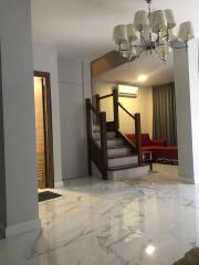 Spacious living room with marble flooring, modern chandelier, and wooden staircase